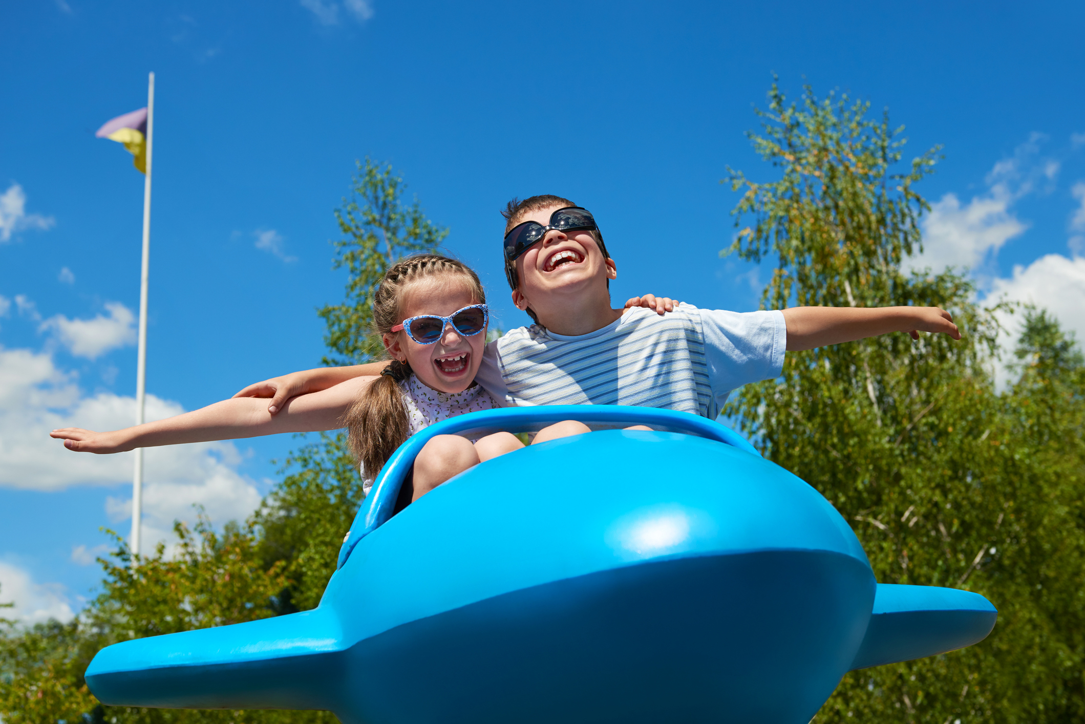 child girl and boy fly on blue plane attraction in city park, happy childhood, summer vacation concept