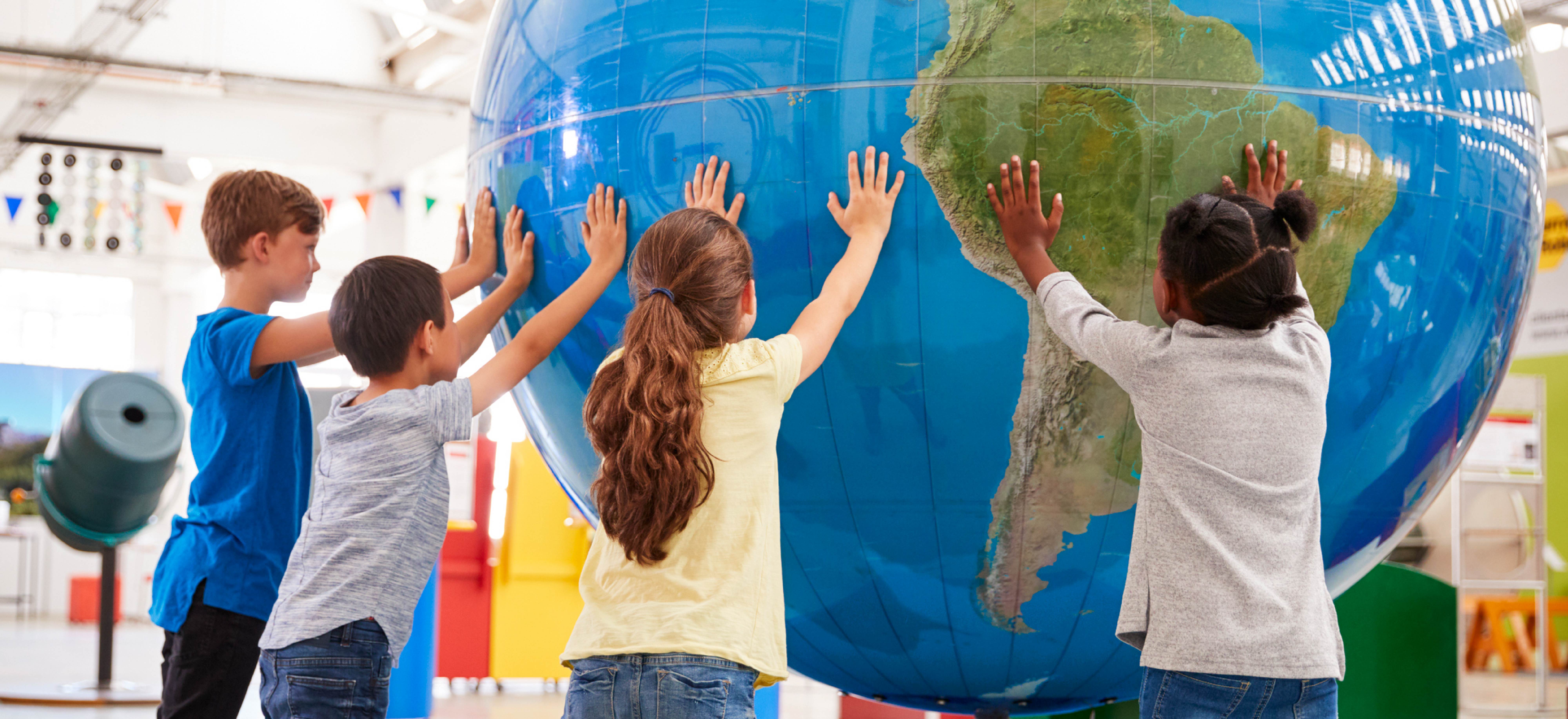 children surrounding a large globe with their hands up against it
